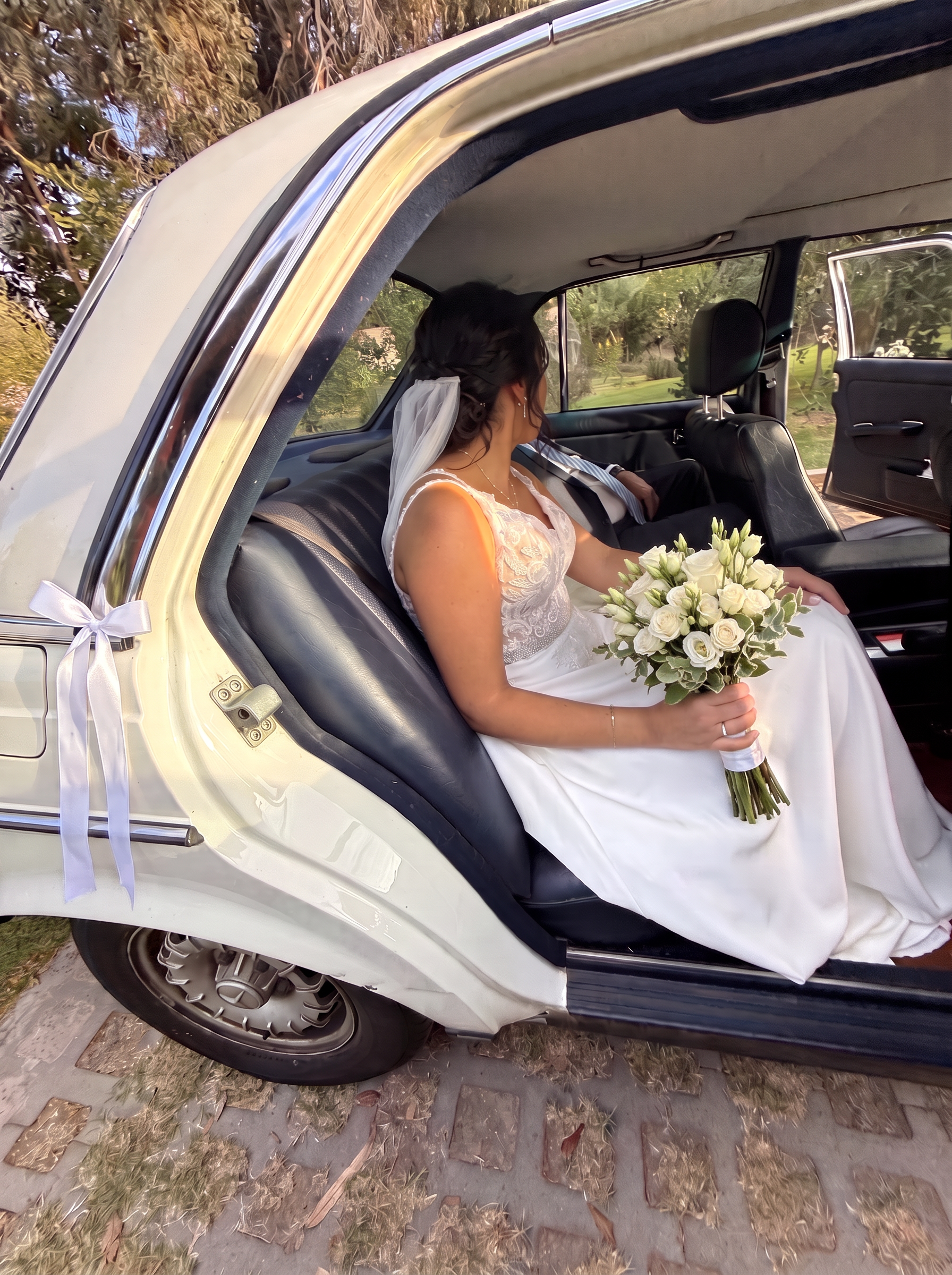 Novia sentada en el asiento trasero del Mercedes-Benz 230 E con su ramo